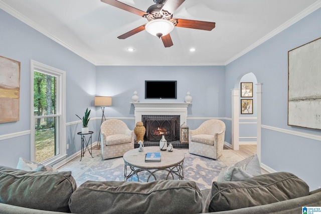 living room with ceiling fan, ornamental molding, a brick fireplace, and light hardwood / wood-style flooring