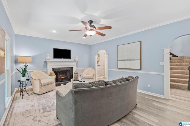 living room with a brick fireplace, crown molding, light hardwood / wood-style flooring, and ceiling fan