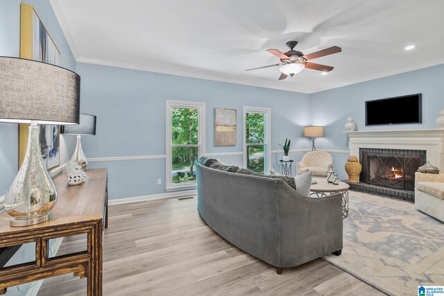 living room with a brick fireplace, ornamental molding, light hardwood / wood-style floors, and ceiling fan