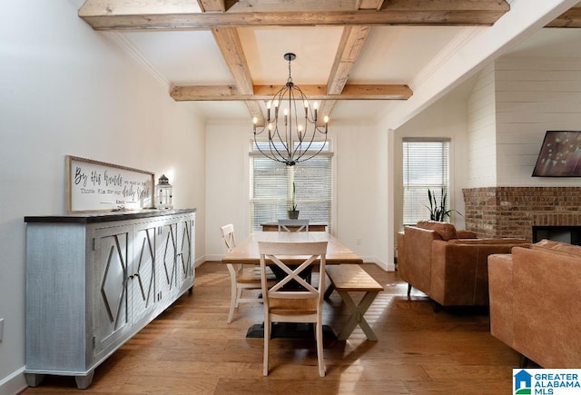 dining space featuring wood-type flooring, beamed ceiling, an inviting chandelier, and a fireplace