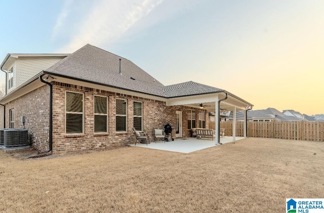 back house at dusk featuring ceiling fan, a lawn, and a patio area