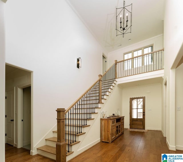 staircase featuring crown molding, a towering ceiling, a chandelier, and hardwood / wood-style flooring