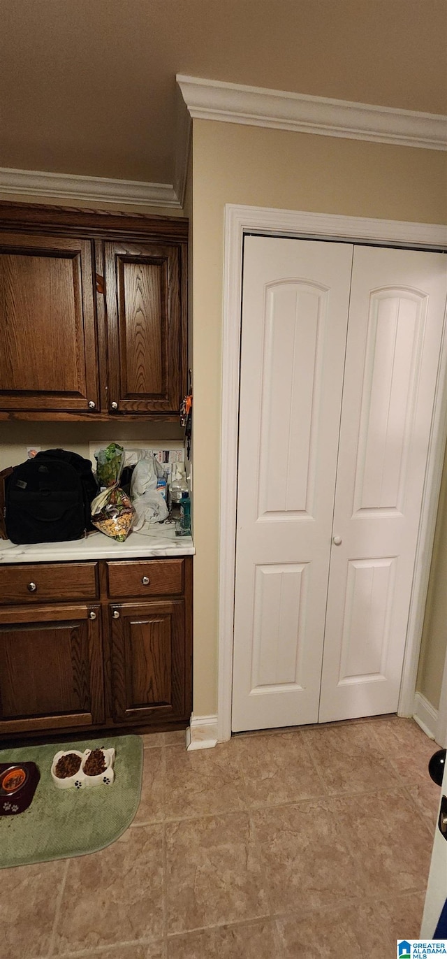 kitchen featuring dark brown cabinetry, ornamental molding, and light tile floors