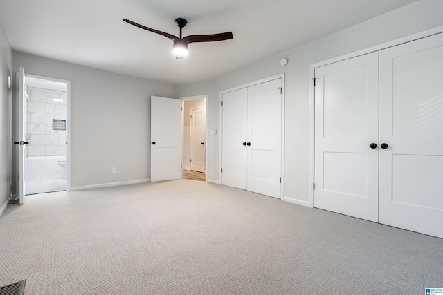 unfurnished bedroom featuring ensuite bathroom, ceiling fan, light carpet, and multiple closets