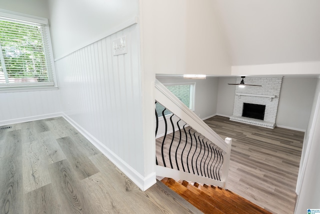 staircase featuring hardwood / wood-style flooring, a brick fireplace, and ceiling fan