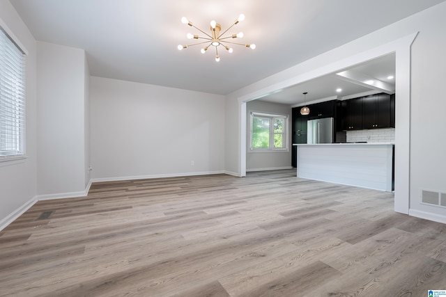 unfurnished living room featuring a chandelier and light wood-type flooring