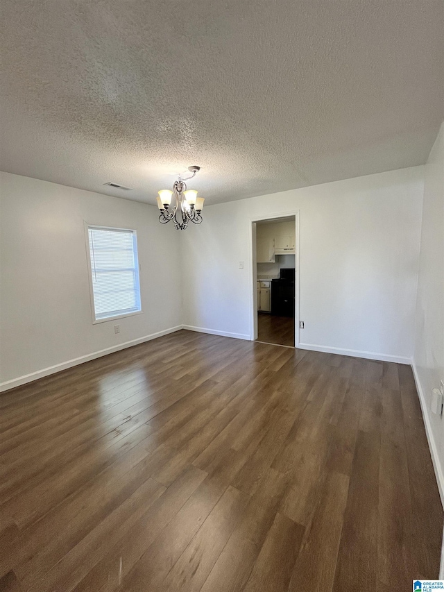 spare room with dark hardwood / wood-style floors, a textured ceiling, and an inviting chandelier