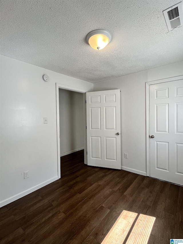 unfurnished bedroom with dark hardwood / wood-style flooring, a textured ceiling, and a closet