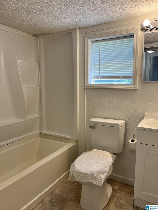 bathroom with a textured ceiling, vanity, tile walls, and bathtub / shower combination