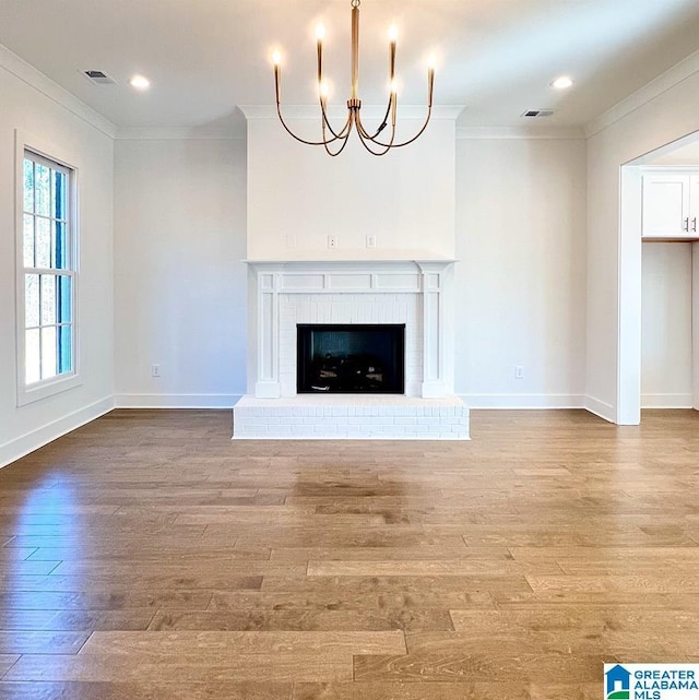 unfurnished living room featuring hardwood / wood-style flooring, crown molding, a brick fireplace, and a notable chandelier