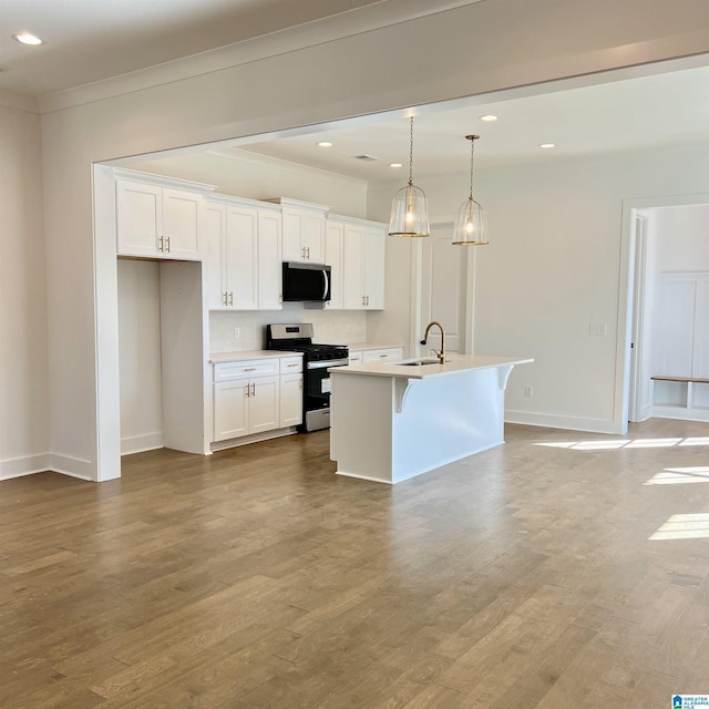 kitchen featuring stainless steel appliances, an island with sink, white cabinets, and decorative light fixtures