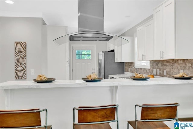 kitchen with decorative backsplash, stainless steel fridge, a kitchen bar, white cabinetry, and island exhaust hood