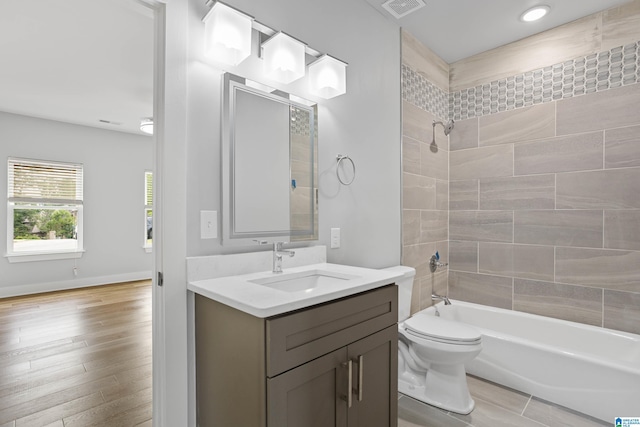 full bathroom featuring vanity, hardwood / wood-style floors, tiled shower / bath combo, and toilet