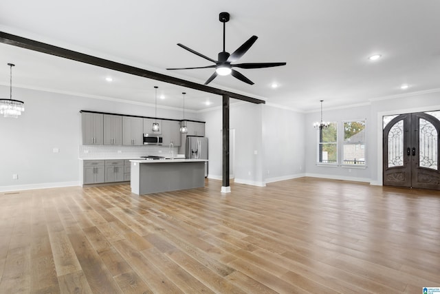 unfurnished living room with ceiling fan with notable chandelier, beamed ceiling, ornamental molding, light hardwood / wood-style floors, and french doors