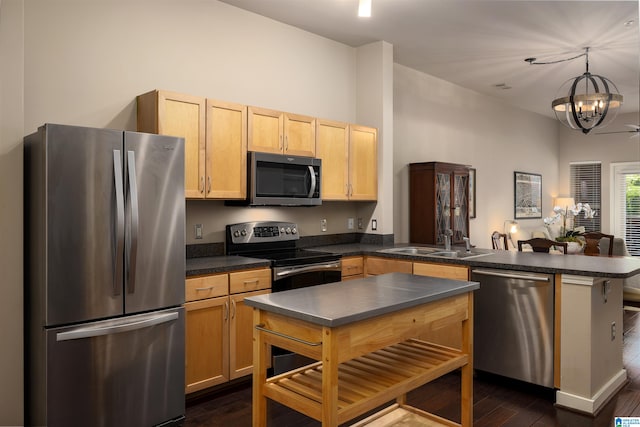 kitchen with dark hardwood / wood-style flooring, appliances with stainless steel finishes, kitchen peninsula, a notable chandelier, and sink