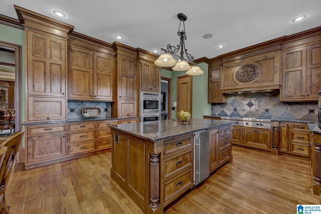 kitchen featuring appliances with stainless steel finishes, a kitchen island, hanging light fixtures, and dark stone counters