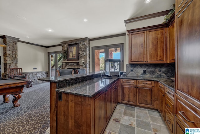 kitchen featuring a fireplace, kitchen peninsula, dark stone counters, and french doors