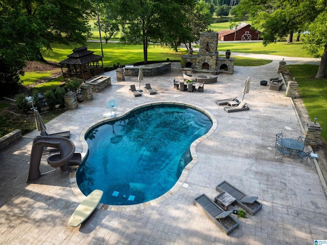 view of swimming pool featuring a yard, a patio area, and an outdoor stone fireplace