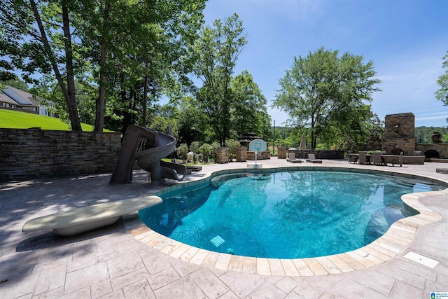 view of swimming pool with a patio area, an outdoor stone fireplace, and a water slide