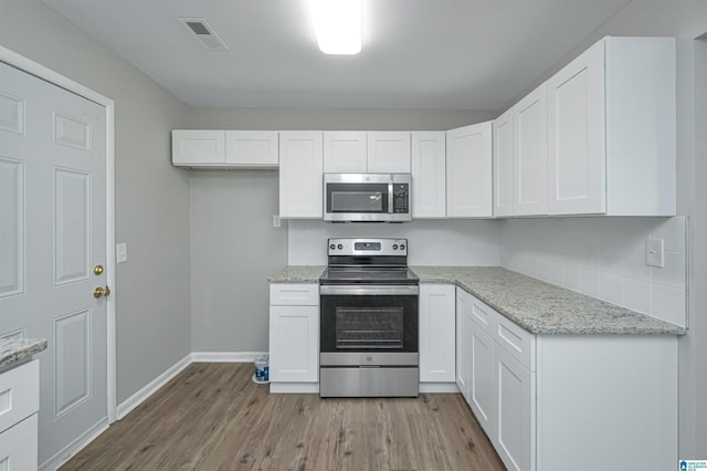 kitchen featuring white cabinetry, stainless steel appliances, light stone counters, and light wood-type flooring