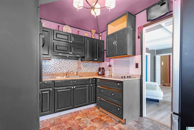 kitchen featuring light stone countertops, black electric stovetop, tasteful backsplash, sink, and a chandelier