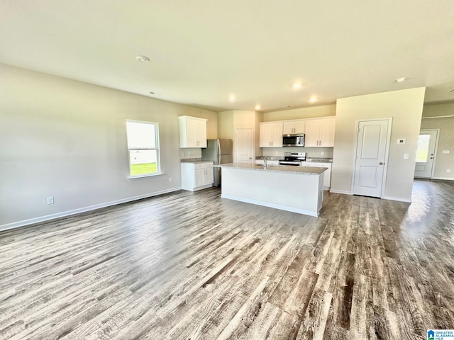 kitchen with white cabinets, a center island with sink, light wood-type flooring, appliances with stainless steel finishes, and light stone counters