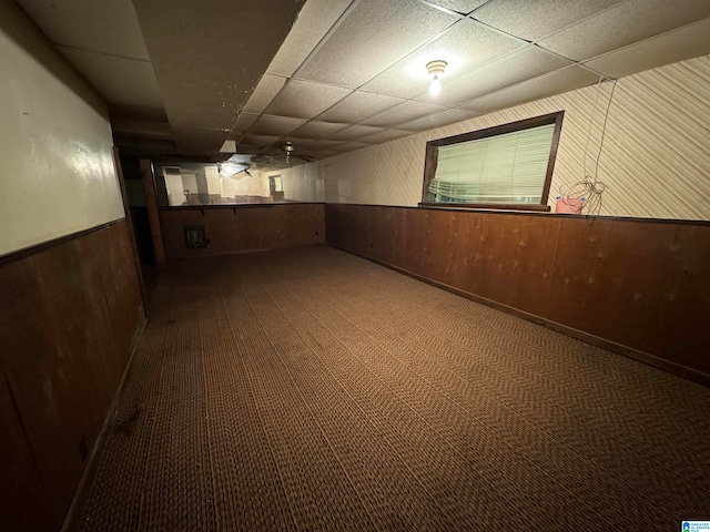 basement with carpet flooring, a drop ceiling, and wood walls