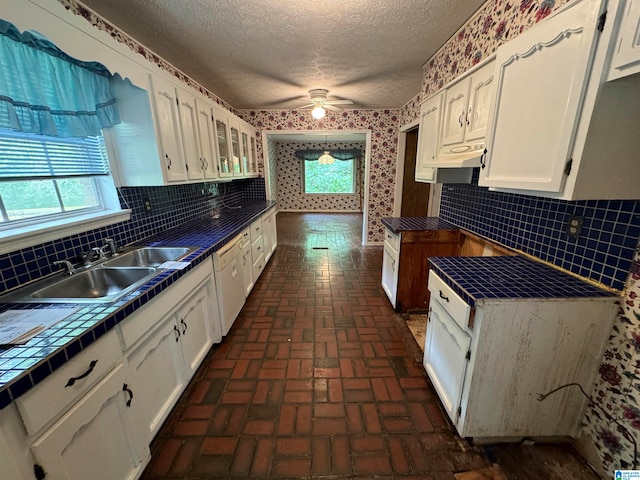 kitchen with tile countertops, white cabinets, sink, a textured ceiling, and tasteful backsplash