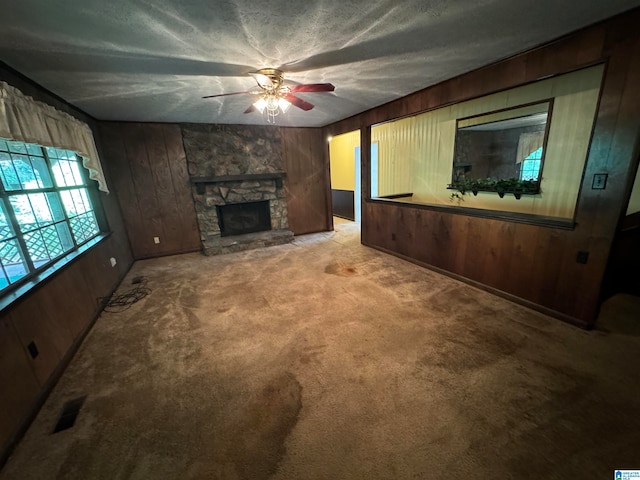 carpeted living room with wood walls, a fireplace, ceiling fan, and a textured ceiling