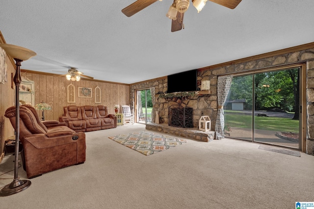 carpeted living room with ceiling fan, wood walls, crown molding, and a fireplace