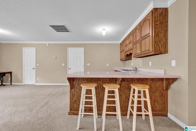 kitchen with kitchen peninsula, sink, light colored carpet, and ornamental molding