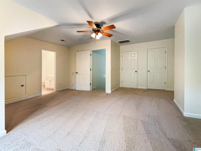 interior space with ceiling fan, light carpet, connected bathroom, and two closets