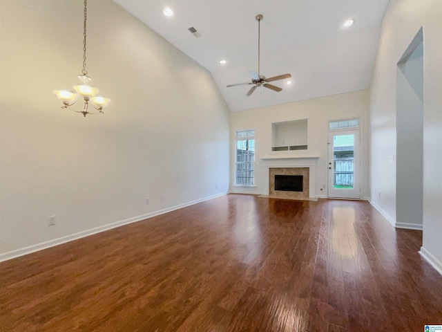 unfurnished living room with dark hardwood / wood-style flooring, ceiling fan with notable chandelier, high vaulted ceiling, and a tiled fireplace