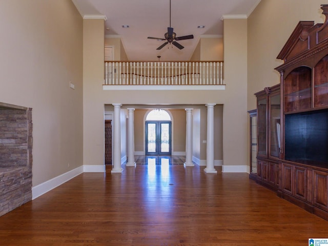 unfurnished living room featuring dark hardwood / wood-style floors, ceiling fan, crown molding, ornate columns, and a high ceiling