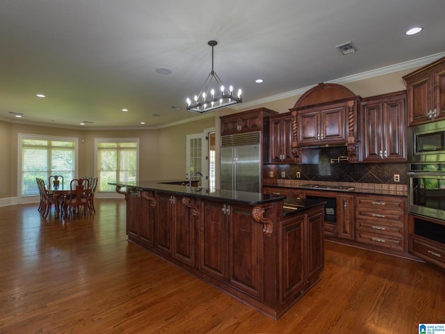 kitchen featuring an inviting chandelier, dark hardwood / wood-style floors, backsplash, a kitchen island with sink, and built in appliances