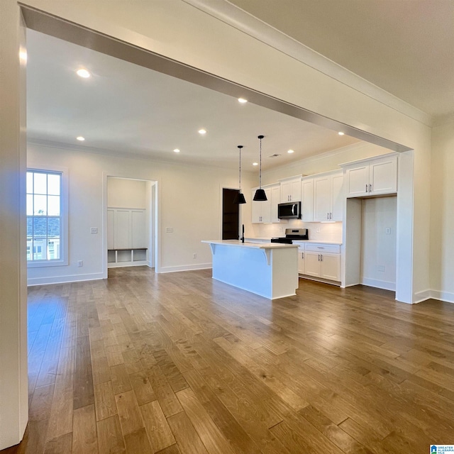 kitchen with a kitchen island with sink, hanging light fixtures, white cabinetry, and appliances with stainless steel finishes