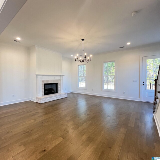 unfurnished living room with a fireplace, plenty of natural light, dark hardwood / wood-style flooring, and a chandelier