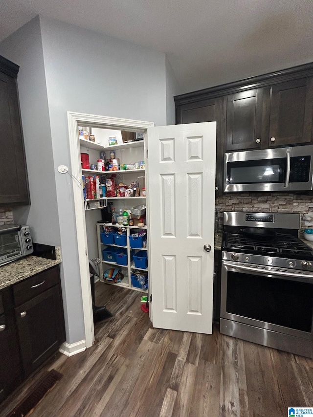 kitchen featuring appliances with stainless steel finishes, dark brown cabinets, dark hardwood / wood-style flooring, and light stone counters