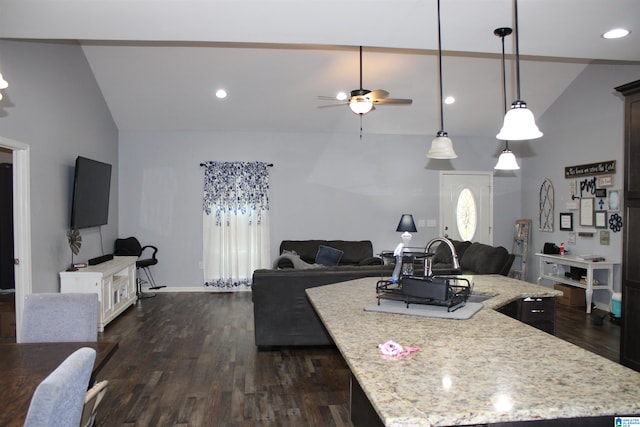 kitchen with dark wood-type flooring, hanging light fixtures, light stone countertops, a kitchen island, and ceiling fan