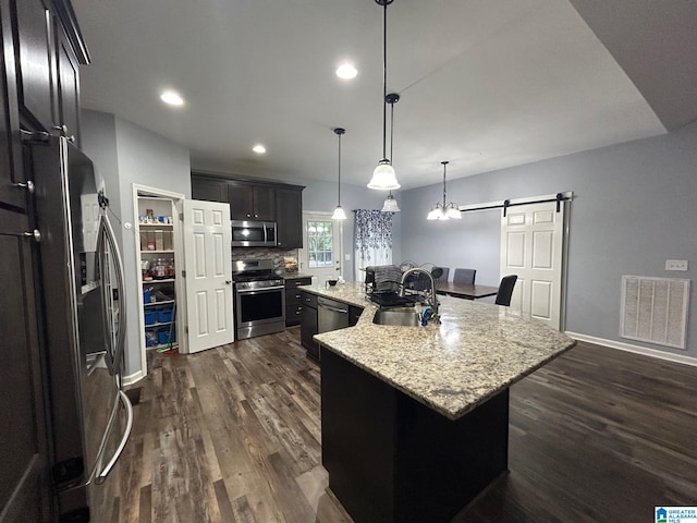 kitchen with a barn door, dark hardwood / wood-style floors, appliances with stainless steel finishes, sink, and a center island