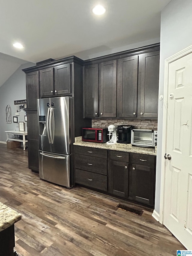 kitchen with tasteful backsplash, stainless steel fridge with ice dispenser, light stone countertops, dark wood-type flooring, and dark brown cabinetry