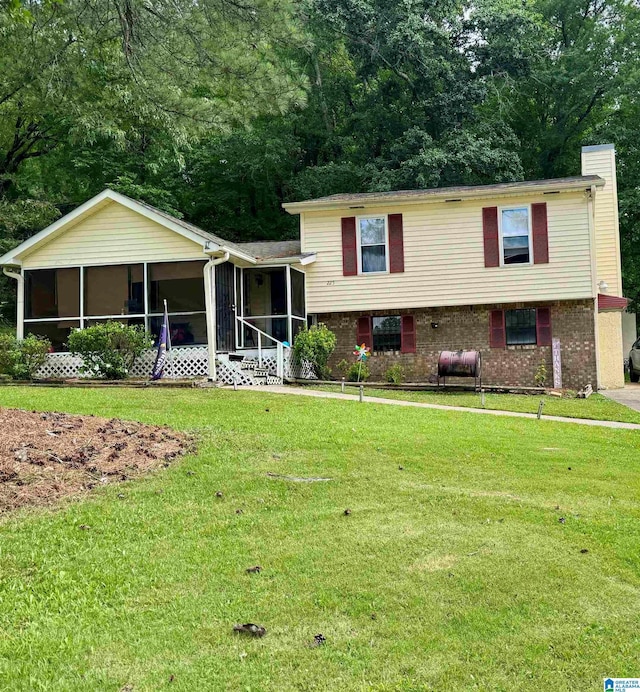 split level home with brick siding, a front lawn, a chimney, and a sunroom