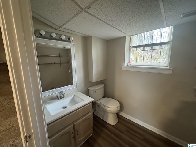 half bath with baseboards, a drop ceiling, toilet, wood finished floors, and vanity