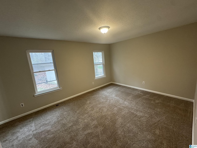 spare room with a textured ceiling, dark carpet, visible vents, and baseboards