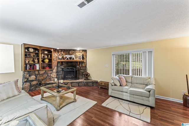 living room featuring built in shelves, dark hardwood / wood-style flooring, a textured ceiling, and a fireplace