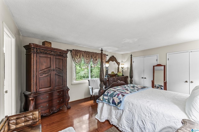 bedroom with two closets, a textured ceiling, and dark hardwood / wood-style flooring