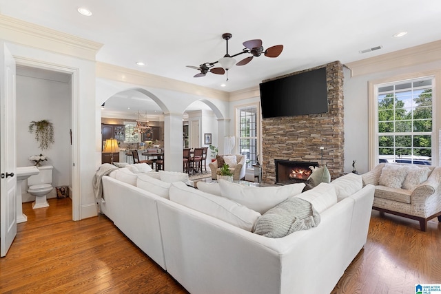 living room with wood-type flooring, a stone fireplace, and ceiling fan