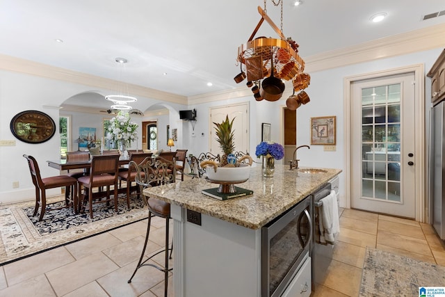 kitchen featuring sink, a breakfast bar area, hanging light fixtures, a center island with sink, and ornamental molding