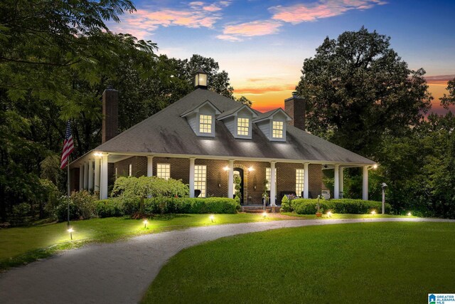 cape cod-style house featuring a porch and a lawn