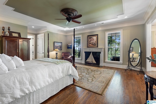 bedroom featuring dark hardwood / wood-style floors, ceiling fan, ornamental molding, and a tray ceiling